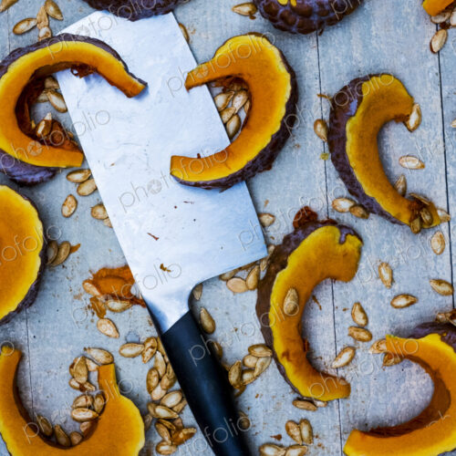High angle close up of cleaver and slices of pumpkin on blue background. High angle close up of cleaver and slices of pumpkin on blue background.