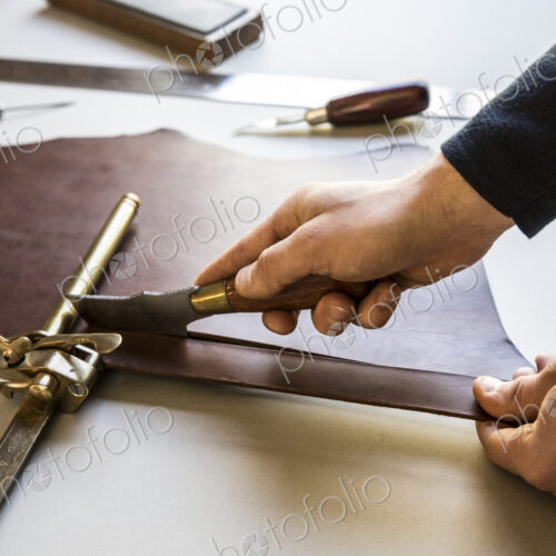 High angle close up of craftsman making brown leather camera strap, clamping the…