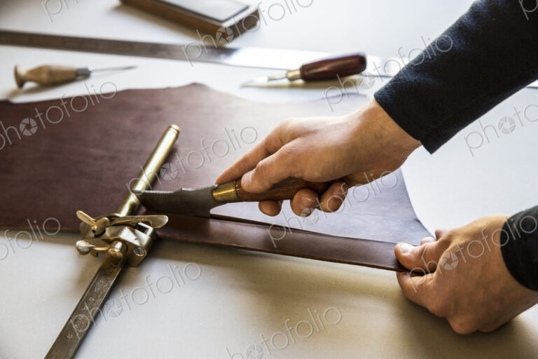 High angle close up of craftsman making brown leather camera strap, clamping the…