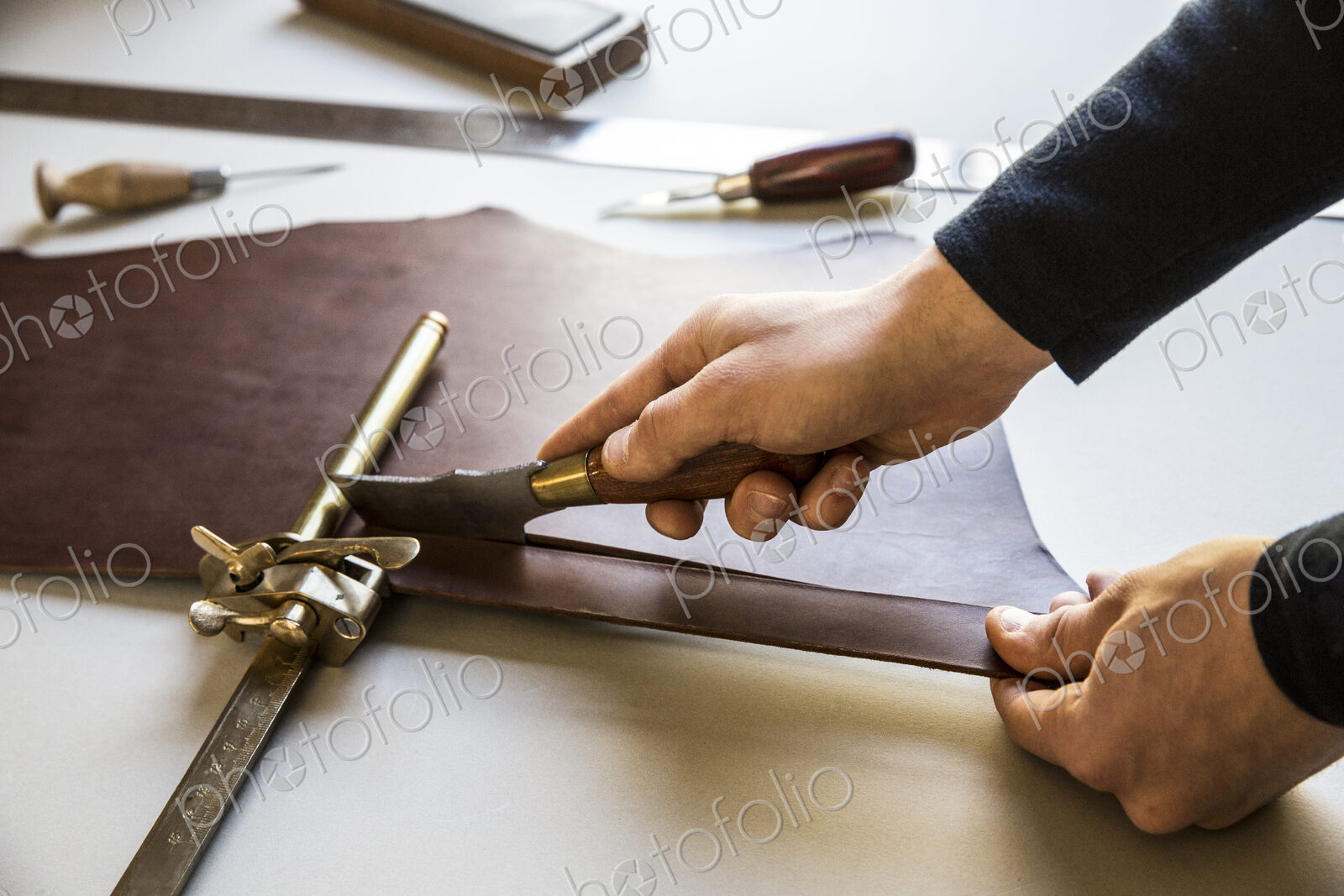 High angle close up of craftsman making brown leather camera strap, clamping the…
