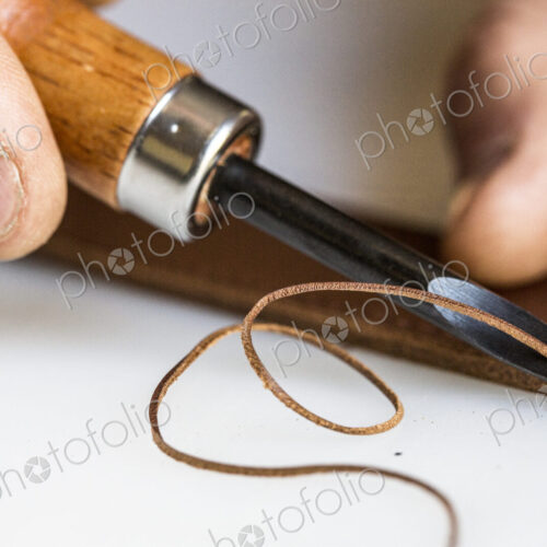 High angle close up of craftsman making brown leather camera strap, using a forked… High angle close up of craftsman making brown leather camera strap, using a forked…