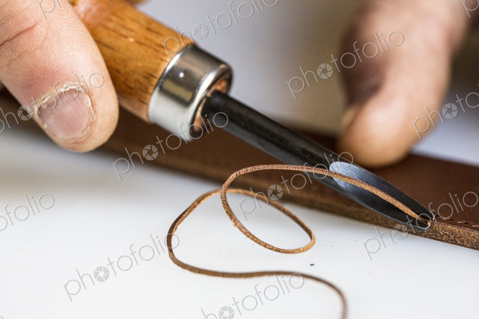 High angle close up of craftsman making brown leather camera strap, using a forked…