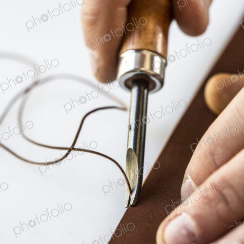 High angle close up of craftsman making brown leather camera strap, using a forked… High angle close up of craftsman making brown leather camera strap, using a forked…