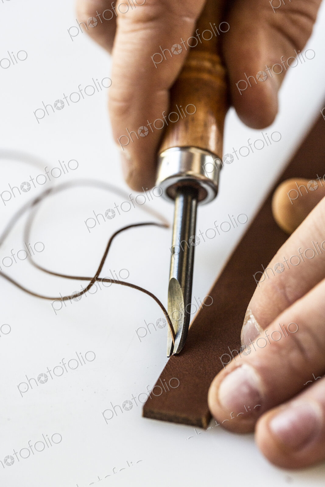 High angle close up of craftsman making brown leather camera strap, using a forked…