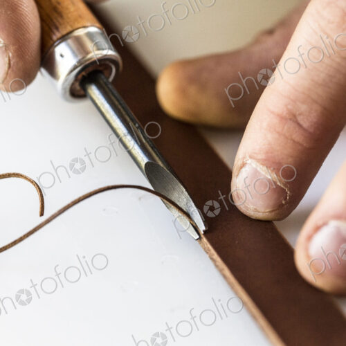High angle close up of craftsman making brown leather camera strap, using a forked… High angle close up of craftsman making brown leather camera strap, using a forked…