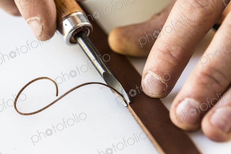 High angle close up of craftsman making brown leather camera strap, using a forked…