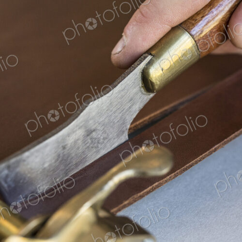 High angle close up of craftsman making brown leather camera strap using a hand tool…