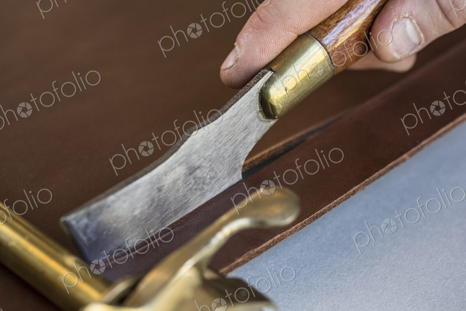 High angle close up of craftsman making brown leather camera strap using a hand tool…