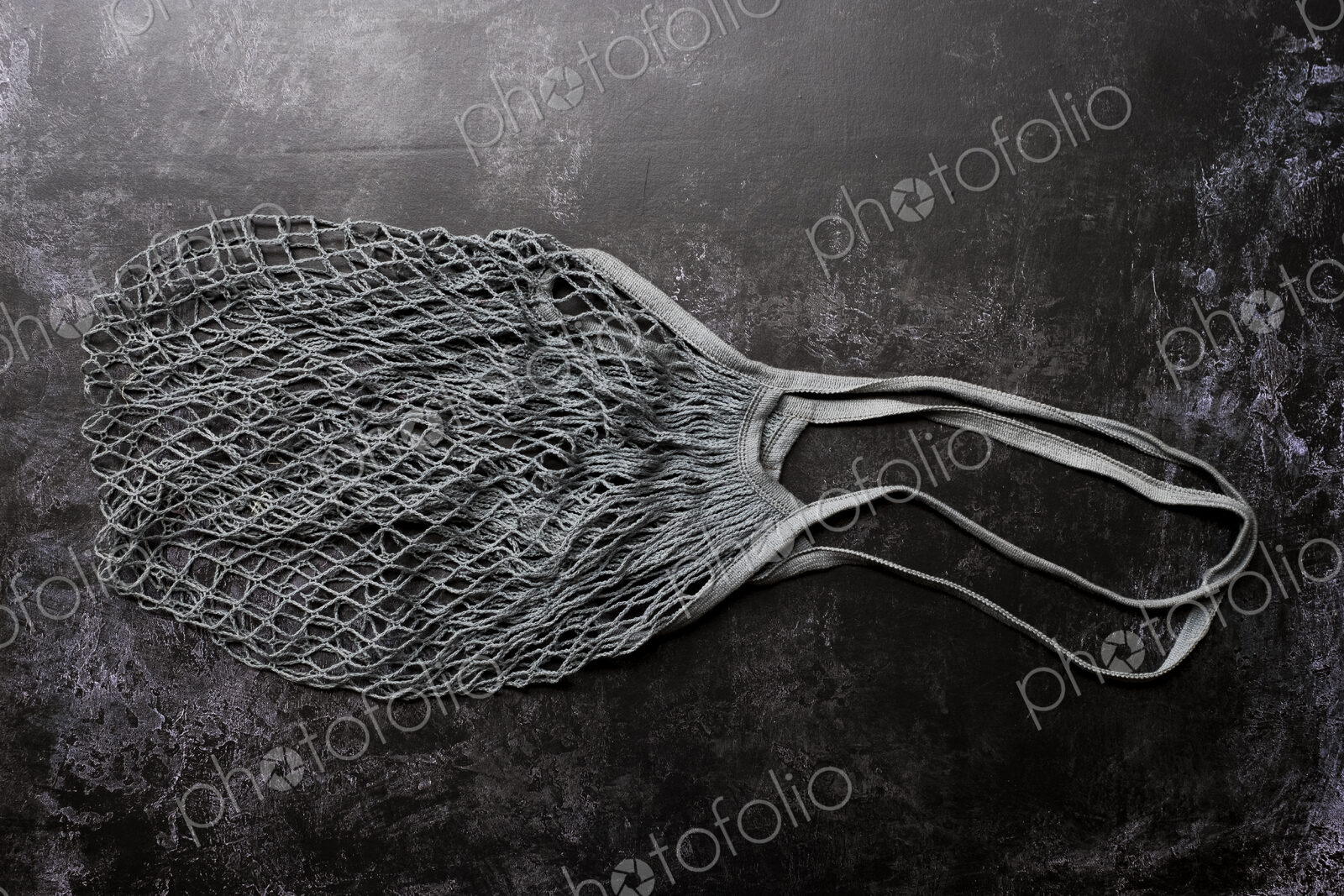 High angle close up of empty grey net bag on black background.