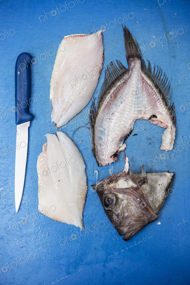 High angle close up of filleted John Dory fish and knife on blue chopping board.
