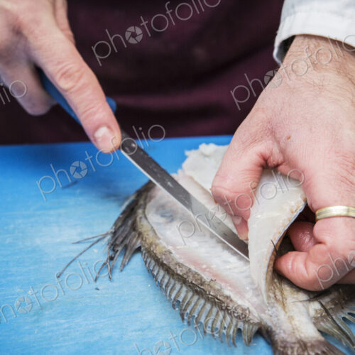 High angle close up of fishmonger filleting John Dory fish with knife on blue chopping…
