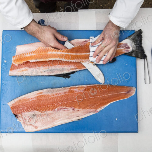 High angle close up of fishmonger standing at a table, cutting and filleting fresh…