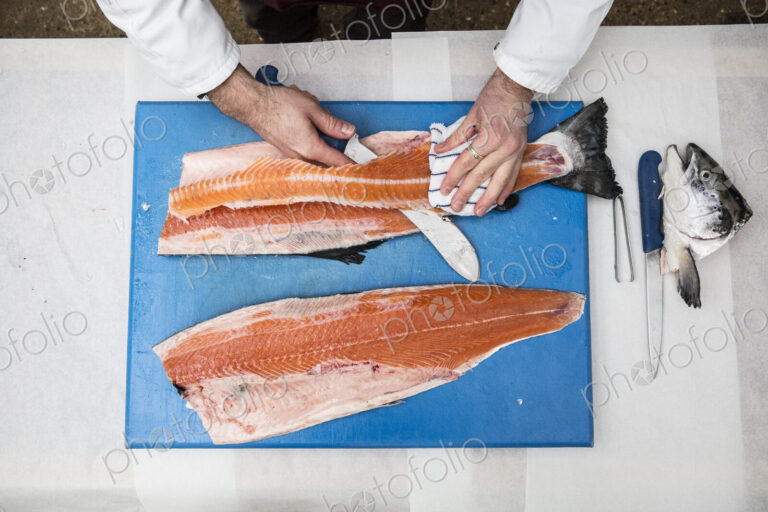High angle close up of fishmonger standing at a table, cutting and filleting fresh…