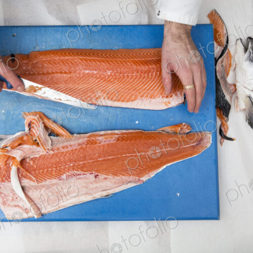 High angle close up of fishmonger standing at a table, cutting and filleting fresh…