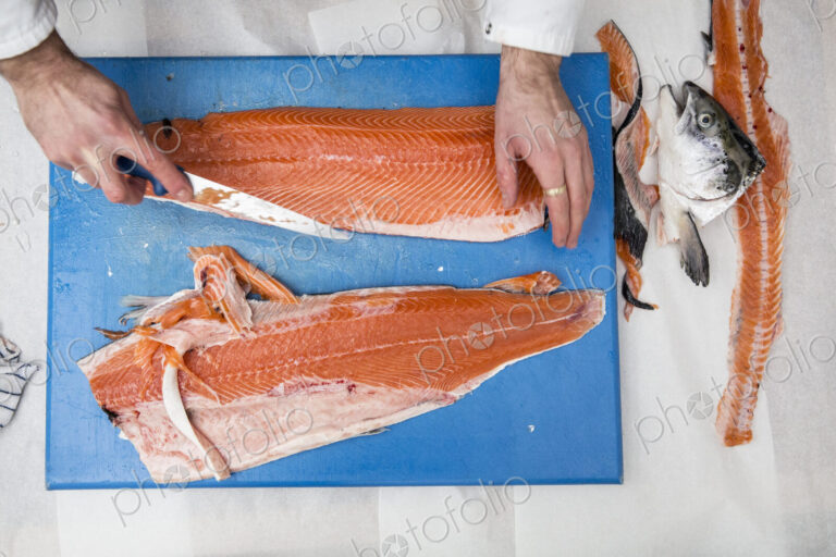 High angle close up of fishmonger standing at a table, cutting and filleting fresh…