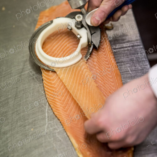 High angle close up of fishmonger using special slicer to thinly slice fillet of salmon. High angle close up of fishmonger using special slicer to thinly slice fillet of salmon.