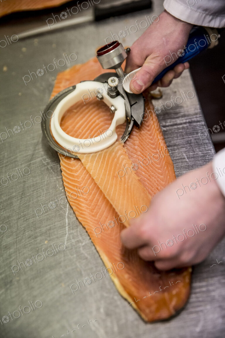 High angle close up of fishmonger using special slicer to thinly slice fillet of salmon.