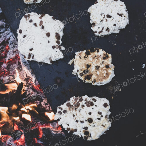 High angle close up of flatbreads cooking on a hot stone over a campfire.