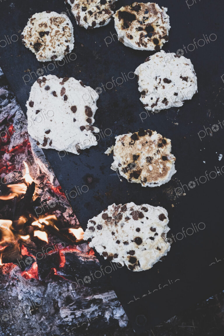 High angle close up of flatbreads cooking on a hot stone over a campfire.