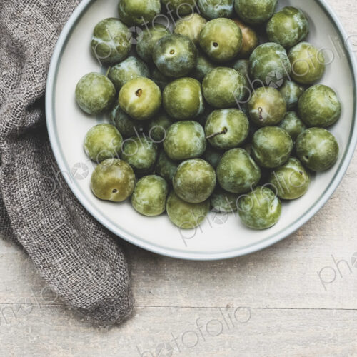 High angle close up of fresh greengages in white bowl.