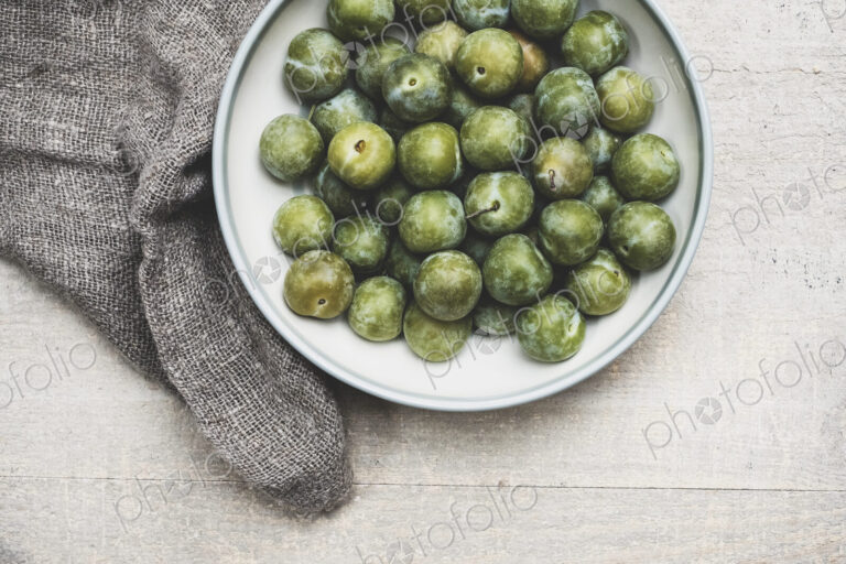High angle close up of fresh greengages in white bowl.