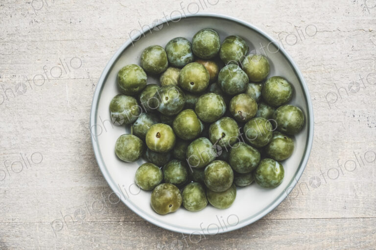 High angle close up of fresh greengages in white bowl.