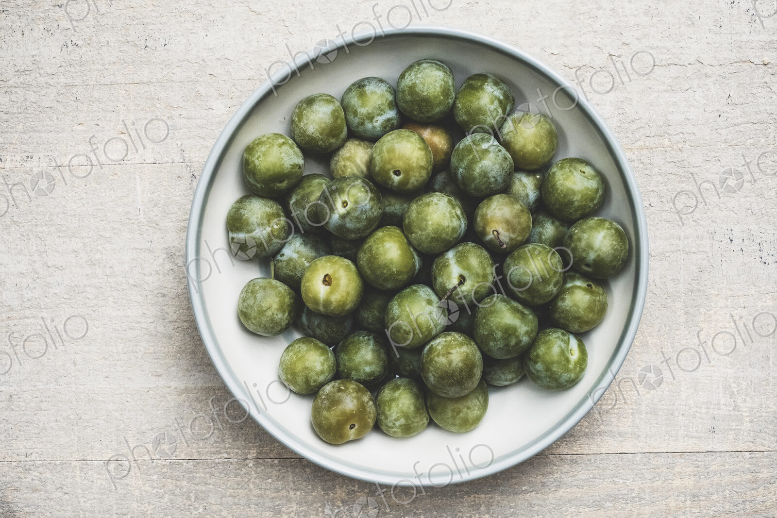 High angle close up of fresh greengages in white bowl.