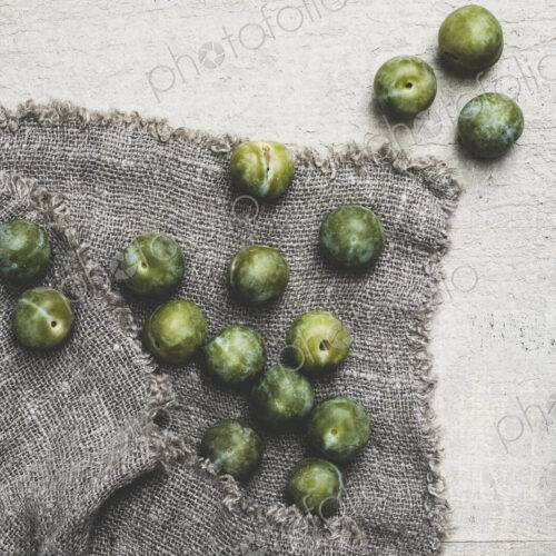 High angle close up of fresh greengages on grey cloth.