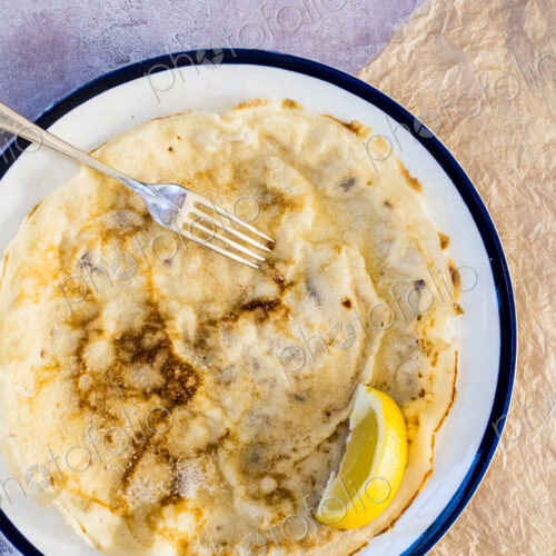 High angle close up of freshly baked crepe with lemon wedge garnish on white plate…