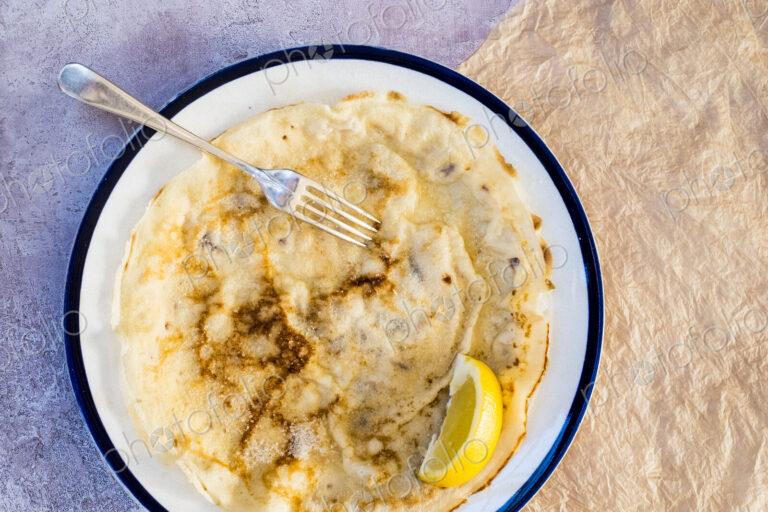High angle close up of freshly baked crepe with lemon wedge garnish on white plate…