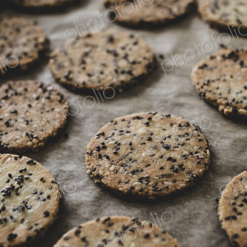 High angle close up of freshly baked seeded crackers on a baking tray.