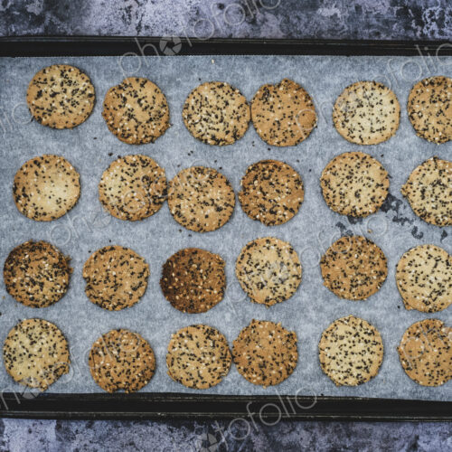 High angle close up of freshly baked seeded crackers on a baking tray. High angle close up of freshly baked seeded crackers on a baking tray.