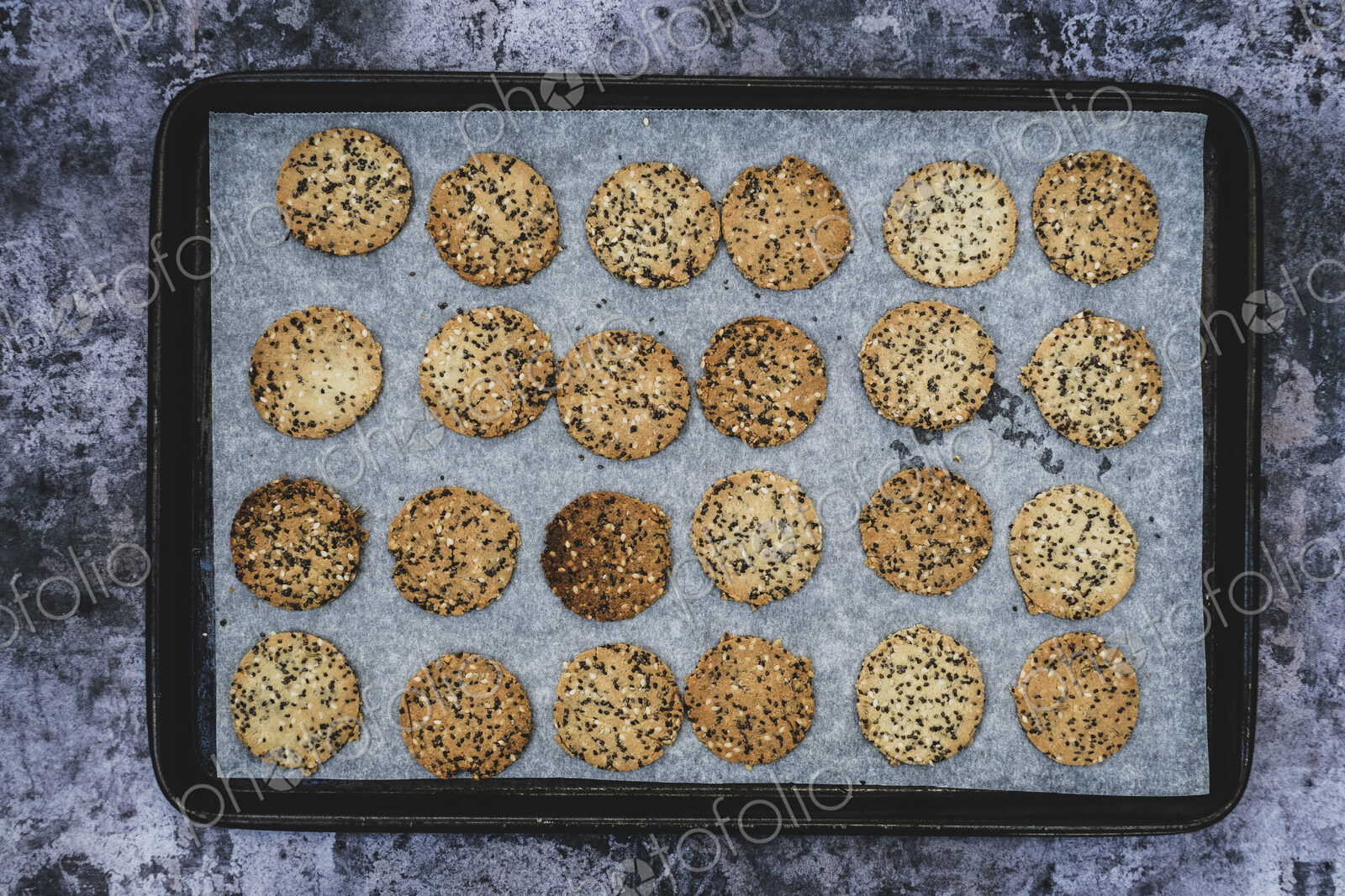 High angle close up of freshly baked seeded crackers on a baking tray.