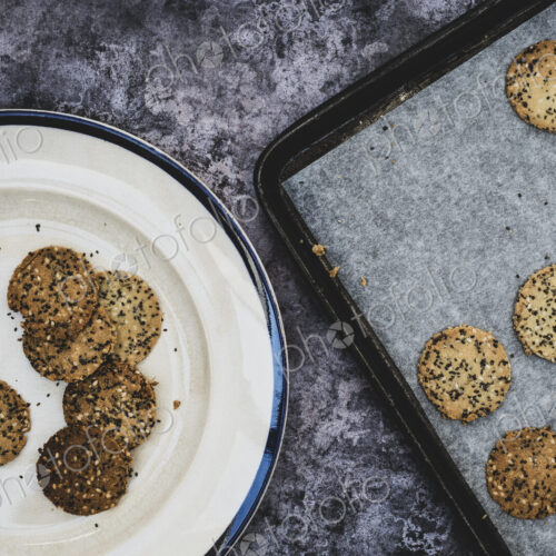 High angle close up of freshly baked seeded crackers on a plate and baking tray. High angle close up of freshly baked seeded crackers on a plate and baking tray.