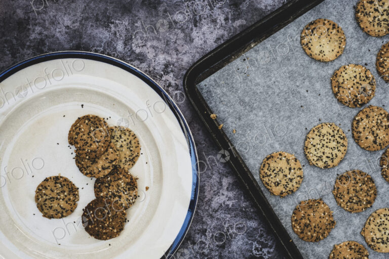 High angle close up of freshly baked seeded crackers on a plate and baking tray.