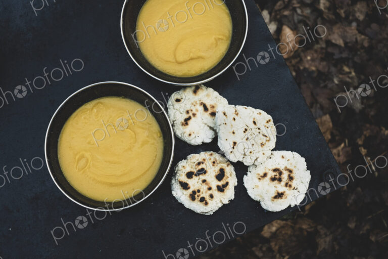 High angle close up of freshly made bread buns and bowls of soup over a campfire.