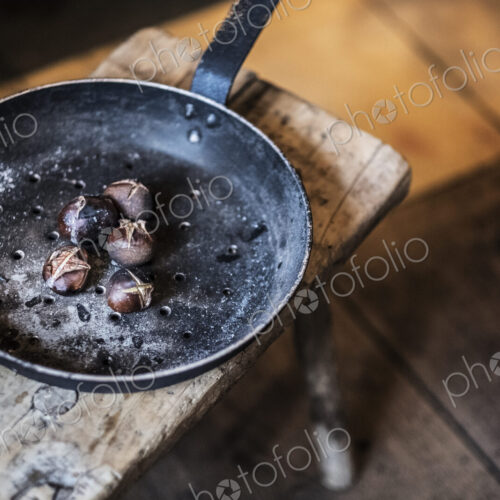High angle close up of frying pan with freshly roasted chestnuts on rustic wooden table. High angle close up of frying pan with freshly roasted chestnuts on rustic wooden table.