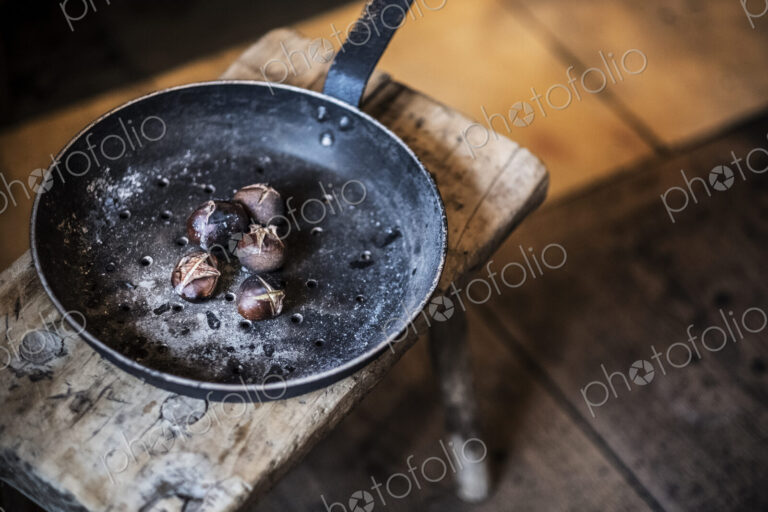 High angle close up of frying pan with freshly roasted chestnuts on rustic wooden table.
