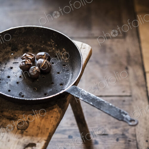 High angle close up of frying pan with freshly roasted chestnuts on rustic wooden table. High angle close up of frying pan with freshly roasted chestnuts on rustic wooden table.