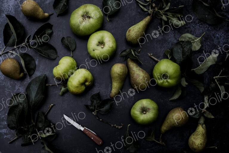 High angle close up of green pears and Bramley apples on black background.