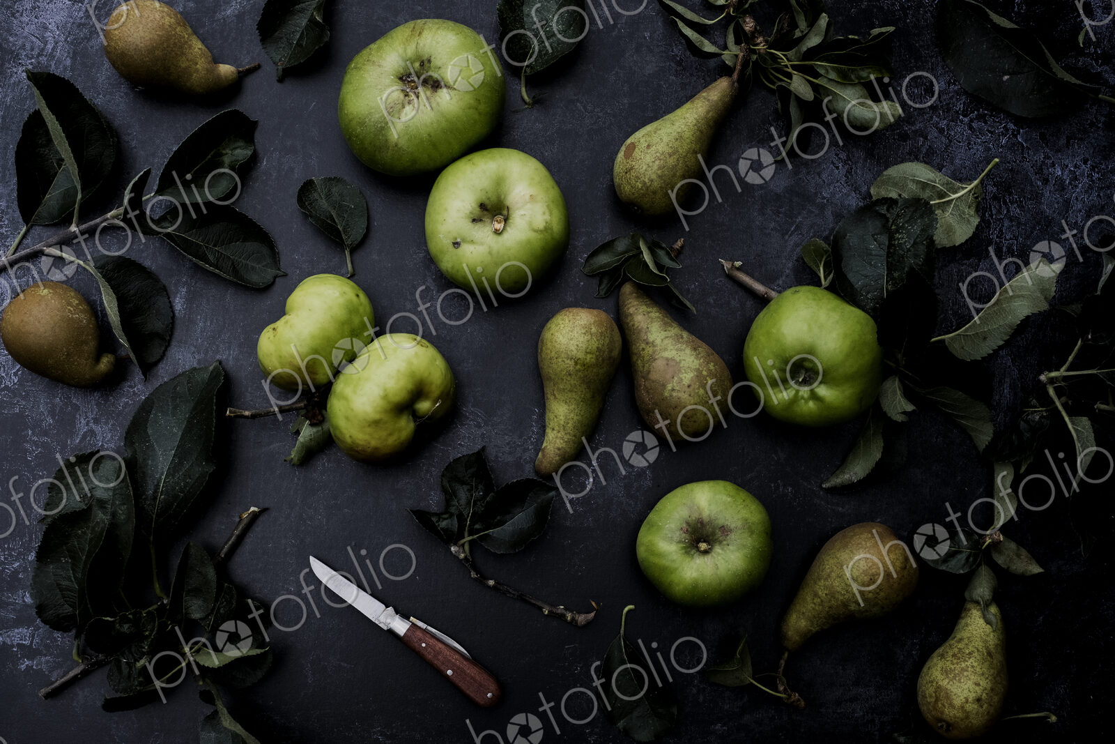 High angle close up of green pears and Bramley apples on black background.