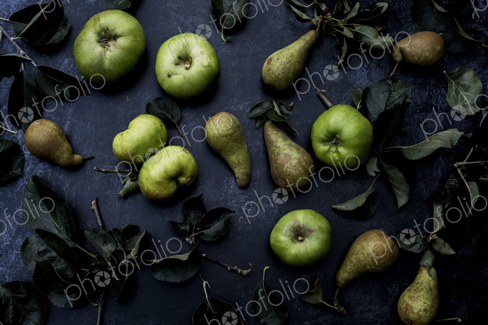 High angle close up of green pears and Bramley apples on black background.