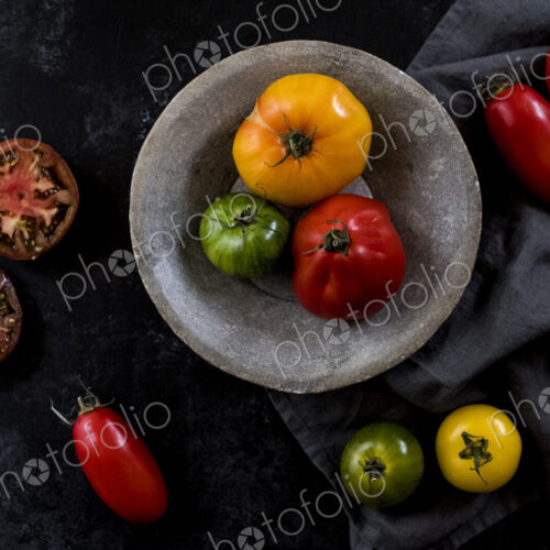 High angle close up of grey plate and cloth and a selection of fresh tomatoes on black… High angle close up of grey plate and cloth and a selection of fresh tomatoes on black…