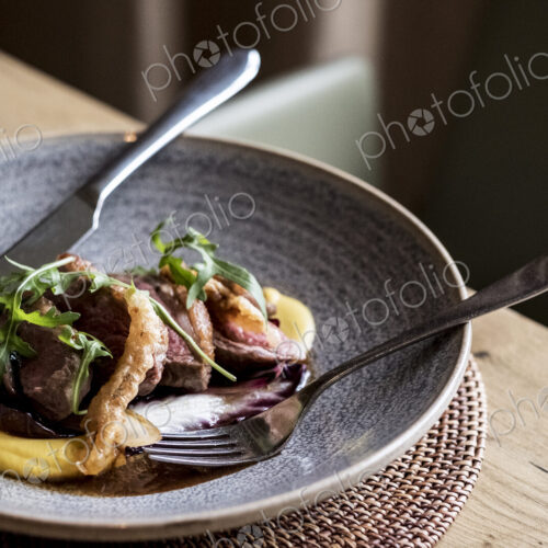 High angle close up of grey plate of meat with mashed potato, crackling and rocket… High angle close up of grey plate of meat with mashed potato, crackling and rocket…