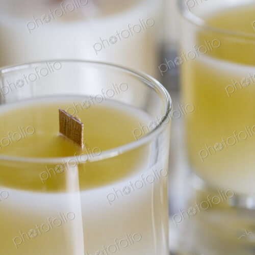 High angle close up of handmade white and yellow jar candles with wooden wick. High angle close up of handmade white and yellow jar candles with wooden wick.