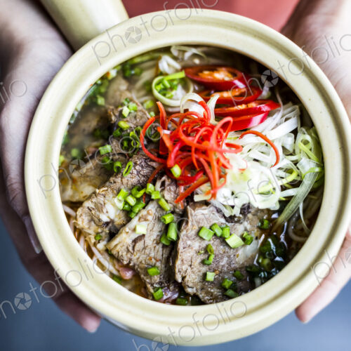 High angle close up of hands holding bowl with Asian soup containing rice vermicelli,… High angle close up of hands holding bowl with Asian soup containing rice vermicelli,…