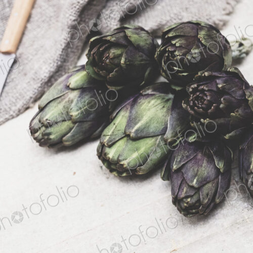 High angle close up of kitchen knife and fresh artichokes on grey background. High angle close up of kitchen knife and fresh artichokes on grey background.