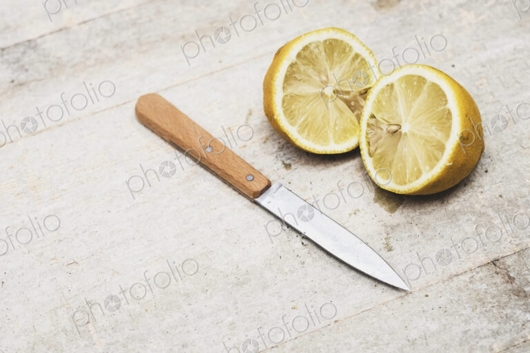 High angle close up of kitchen knife and fresh lemon sliced in half.