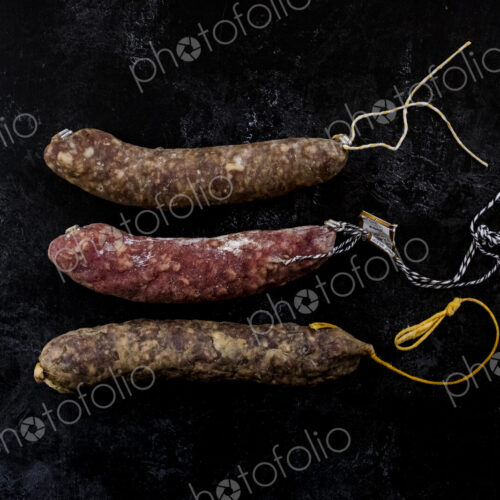 High angle close up of knife and selection of three salamis on black background. High angle close up of knife and selection of three salamis on black background.