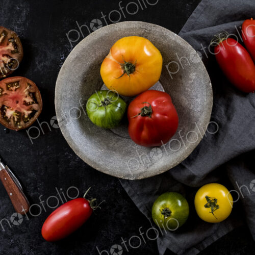 High angle close up of knife, grey plate and cloth and a selection of fresh tomatoes… High angle close up of knife, grey plate and cloth and a selection of fresh tomatoes…